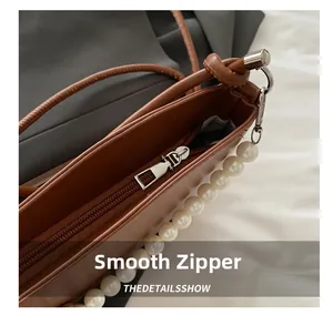 Detail of smooth metal zipper and white pearl decoration on brown leather saddle bag