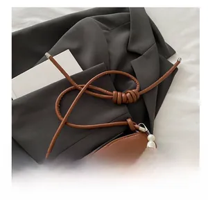 Detail of caramel brown underarm bag with oversized pearl strap and knotted leather cord