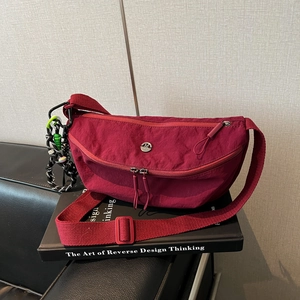 Close-up van wijnrode nylon halve maantas met M-logo en decoratieve kralenhanger aan zijde
