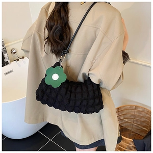 Détail du sac bandoulière noir à texture popcorn avec un charm fleur verte sur modèle