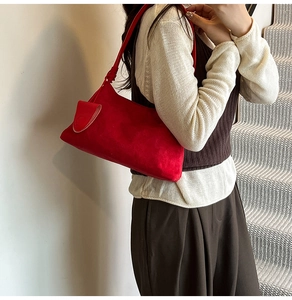 Detailed view of red suede shoulder bag with decorative flap pocket on model in staircase