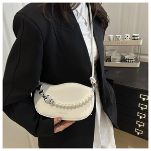 Detail of cream crescent bag with pearl and heart metal chain on model in black suit