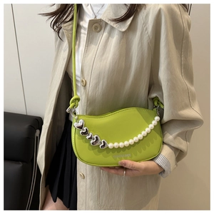 Detail of bright green saddle bag with silver heart chain and pearl accents on shoulder strap