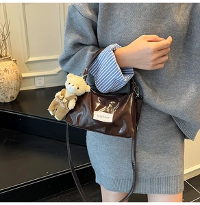 Detail of dark brown glossy patent cloud bag with a cute teddy bear plush charm