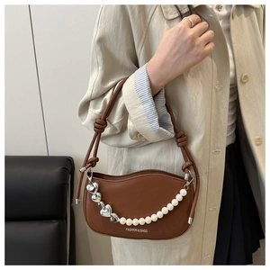 Detail of brown saddle bag with pearl heart chain and twisted strap on model