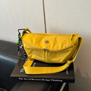 Detail van een gele halvemaanvormige nylon crossbodytas met dubbele rits en een bedeltje