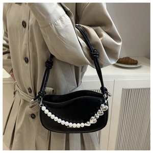 Detail of black underarm bag featuring heart metal charms and pearl chain decoration