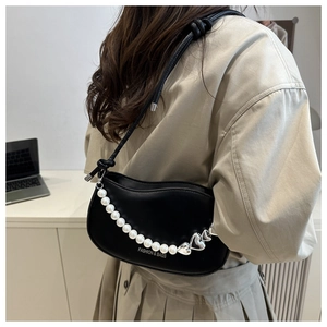 Detail of black leather crescent bag featuring pearl chain and heart charm decoration