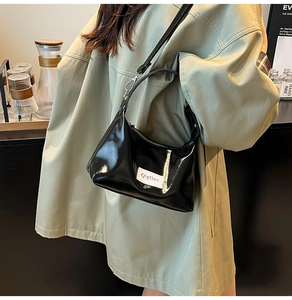 Close-up of black patent leather underarm bag with brand tag worn with a green coat