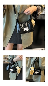Detail of glossy black patent leather shoulder bag with cute brown teddy bear charm