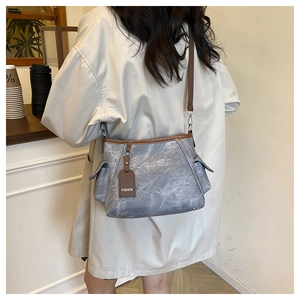 Détail du sac bandoulière gris-bleu avec bordure brune et étiquette FASHION sur manteau