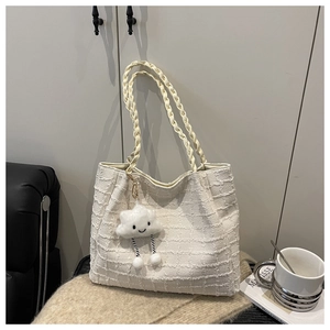 Detail of cream tote bag with woven texture, twisted handle, and plush cloud charm