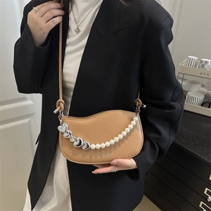 Beige saddle bag with wave edges and decorative heart chain worn with black blazer