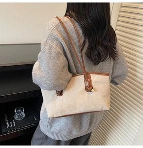 Close-up of beige suede tote bag with brown leather handles worn on a model's shoulder