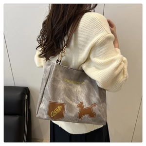 Close-up of grey canvas tote bag with brown leather straps and animal patch on model