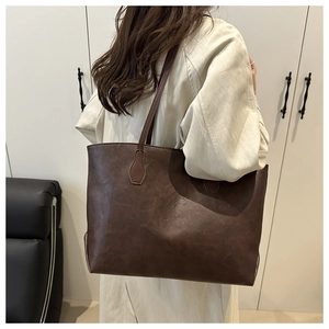 Detail view of a large brown leather tote bag worn by a model in a minimalist room