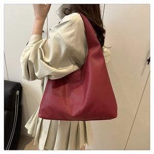 Detail of burgundy textured leather tote bag worn as a shoulder bag on a female model