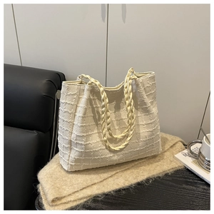 Detail of cream woven tote bag featuring textured fabric and braided rope handles on a table