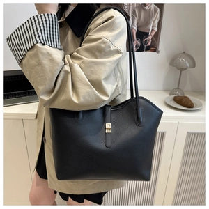Close-up of black lychee grain tote bag with gold metal clasp on a stylish woman