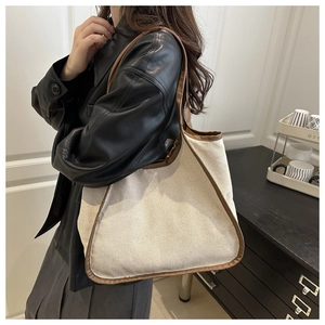 Detailed view of cream canvas tote bag with brown leather trim worn by model in a room
