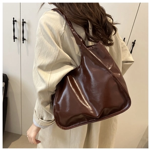 Detail of glossy dark brown tote bag with wide strap and polished leather texture