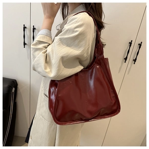 Close-up of minimalist burgundy glossy leather tote bag worn as a shoulder bag