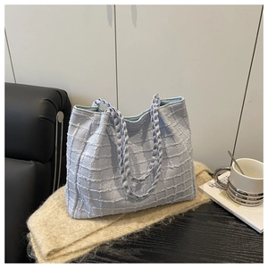 Close-up of light blue tote bag featuring textured tweed fabric and woven satin handles