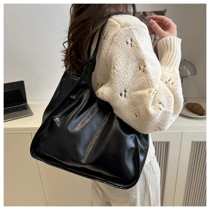 Detailed view of a black pleated shoulder bag worn by a model in a cozy lifestyle setting