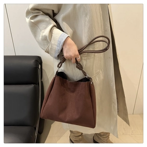 Détail du sac seau vintage en daim marron foncé avec poignée à nœud en cuir et anneaux en métal