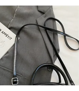 Detail of sleek black patent leather bag with adjustable strap and silver metal buckle