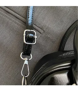 Detail of silver hardware buckle and glossy black leather strap on Boston bag