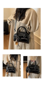 Detail of black glossy Boston bag with round handles and a beige leather charm accessory