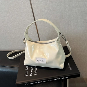 Minimalist beige glossy patent leather handbag with adjustable strap on a book