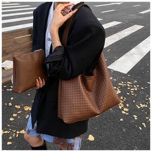 Close-up of brown woven bucket bag and matching pouch on an autumn street background