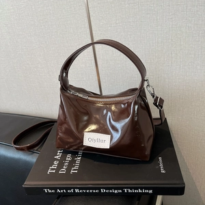 Deep brown patent leather handbag with a top handle and shoulder strap on a book base