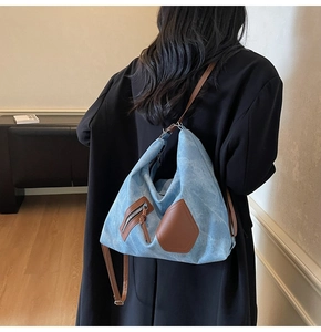 Close-up of light blue denim tote with brown leather trim and vintage zipper detail
