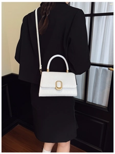 Detail of white crocodile pattern baguette bag with gold metal buckle on black blazer