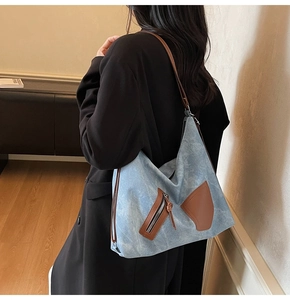 Detail of light blue denim tote bag with brown leather accents and front zipper pocket