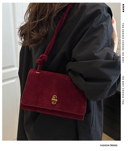 Close-up of burgundy suede crossbody bag with gold metal clasp on a black shirt