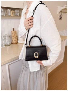 Classic black crocodile pattern handbag with gold metal clasp on a model in a kitchen