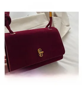 Close-up of burgundy suede handbag featuring a gold twist lock and decorative knot