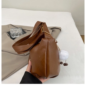 Close-up of caramel leather bag with metal zipper detail and white plush ball charm