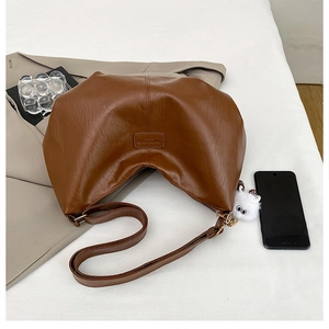 Detail of a brown pleated crescent bag with leather texture and plush toy pendant