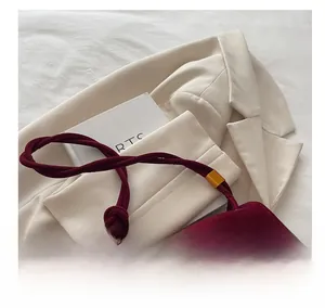 Detail of burgundy suede handbag with woven knot handle and gold metal lock on beige blazer