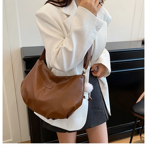 Detail of a brown leather tote bag with a white fluffy charm and wide shoulder strap