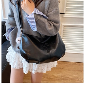 Detail of minimalist black tote bag featuring smooth leather texture and white pompom charm