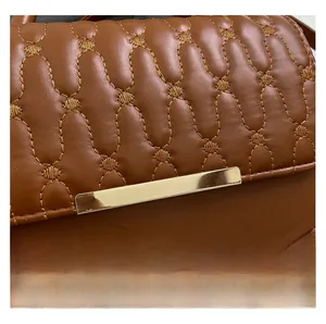 Detalle de textura de cuero acolchado marrón con costuras onduladas y metal dorado
