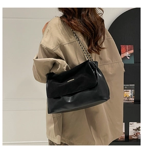 Modern black leather crossbody bag with gold chain strap shown on model from behind