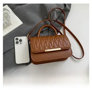 Detalle de bolso bandolera de cuero acolchado marrón con adornos metálicos y asa