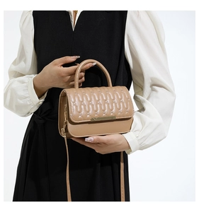 Detalle de bolso bandolera beige con relieve, cierre de metal dorado y asa de mano